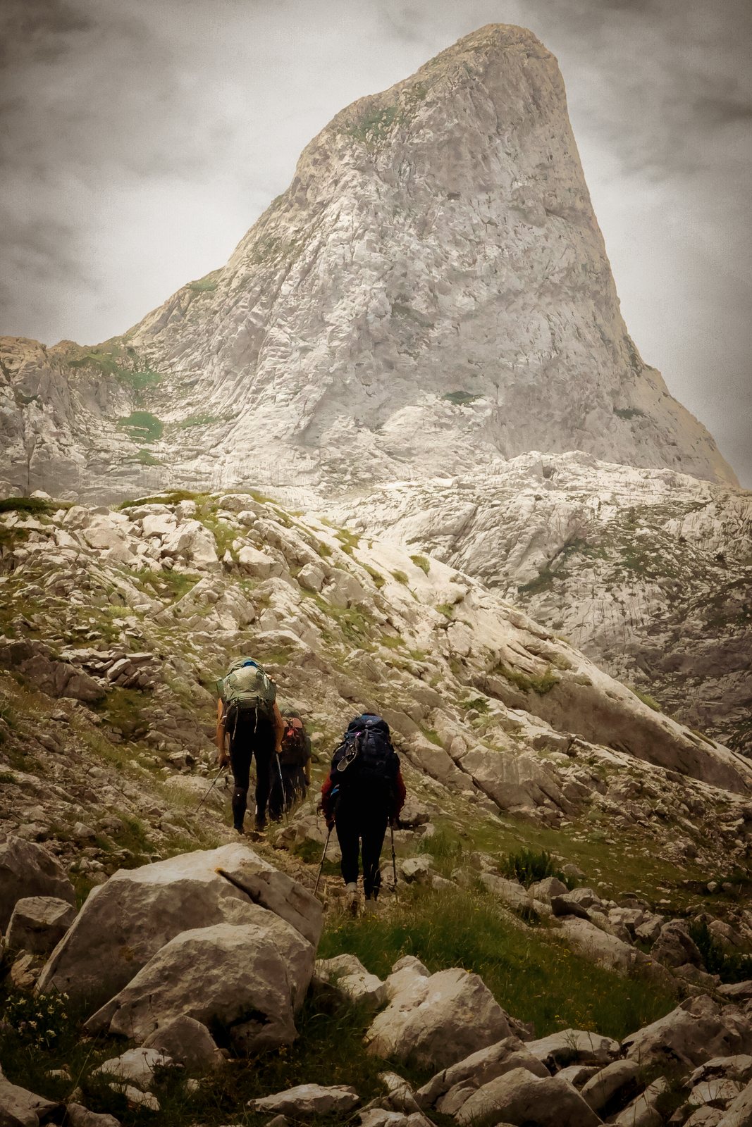 Two hikers climb toward a pointed peak