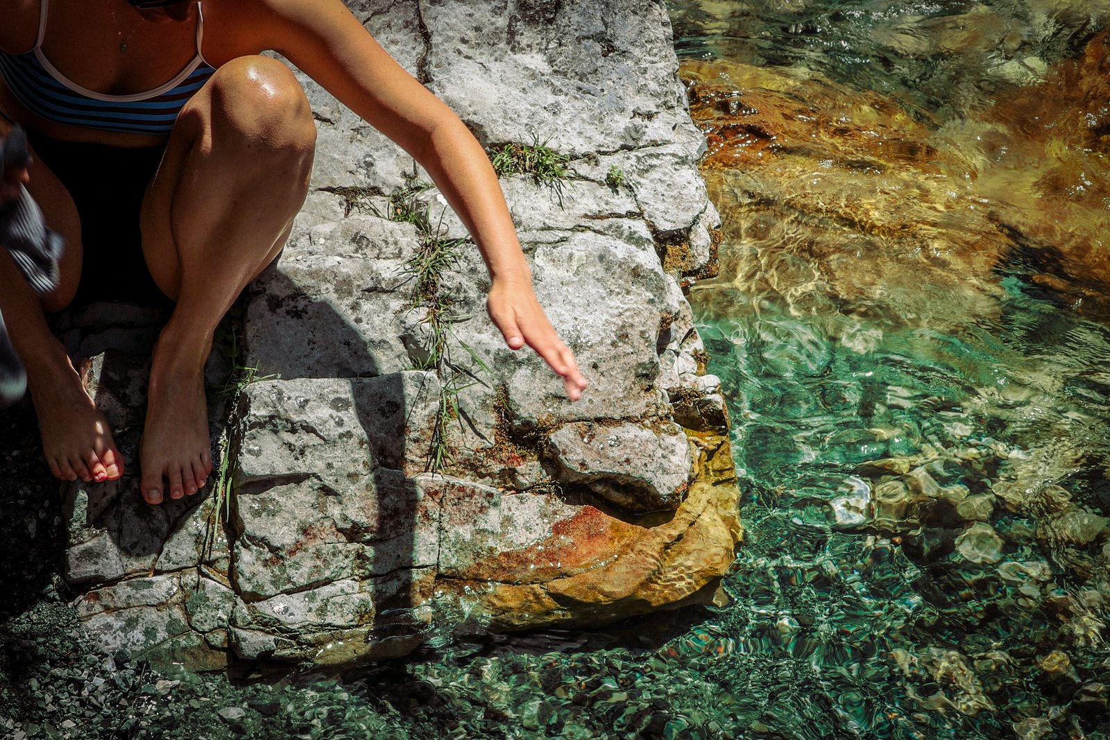 A hiker sitting on a rock beside clear green water