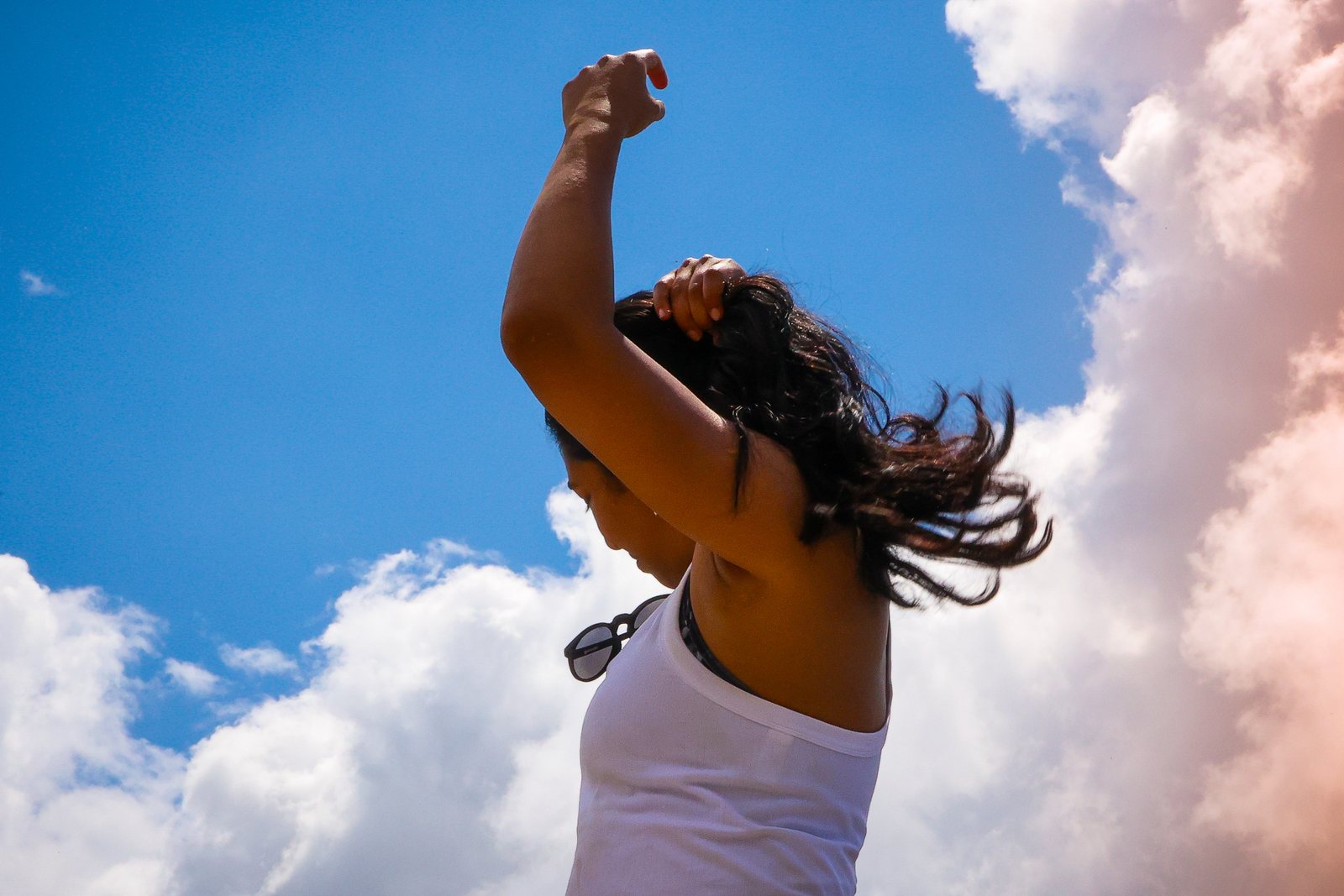 A hiker throws an arm up against blue sky and cloud