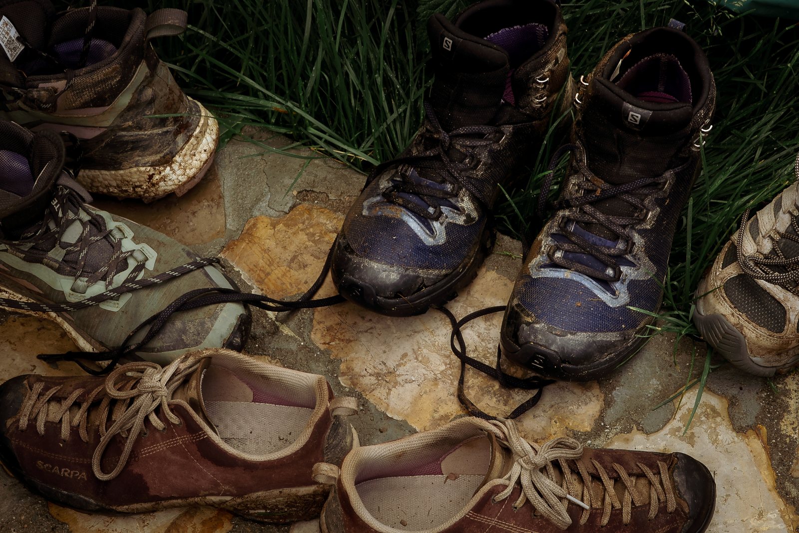A pile of worn hiking boots on a stone floor