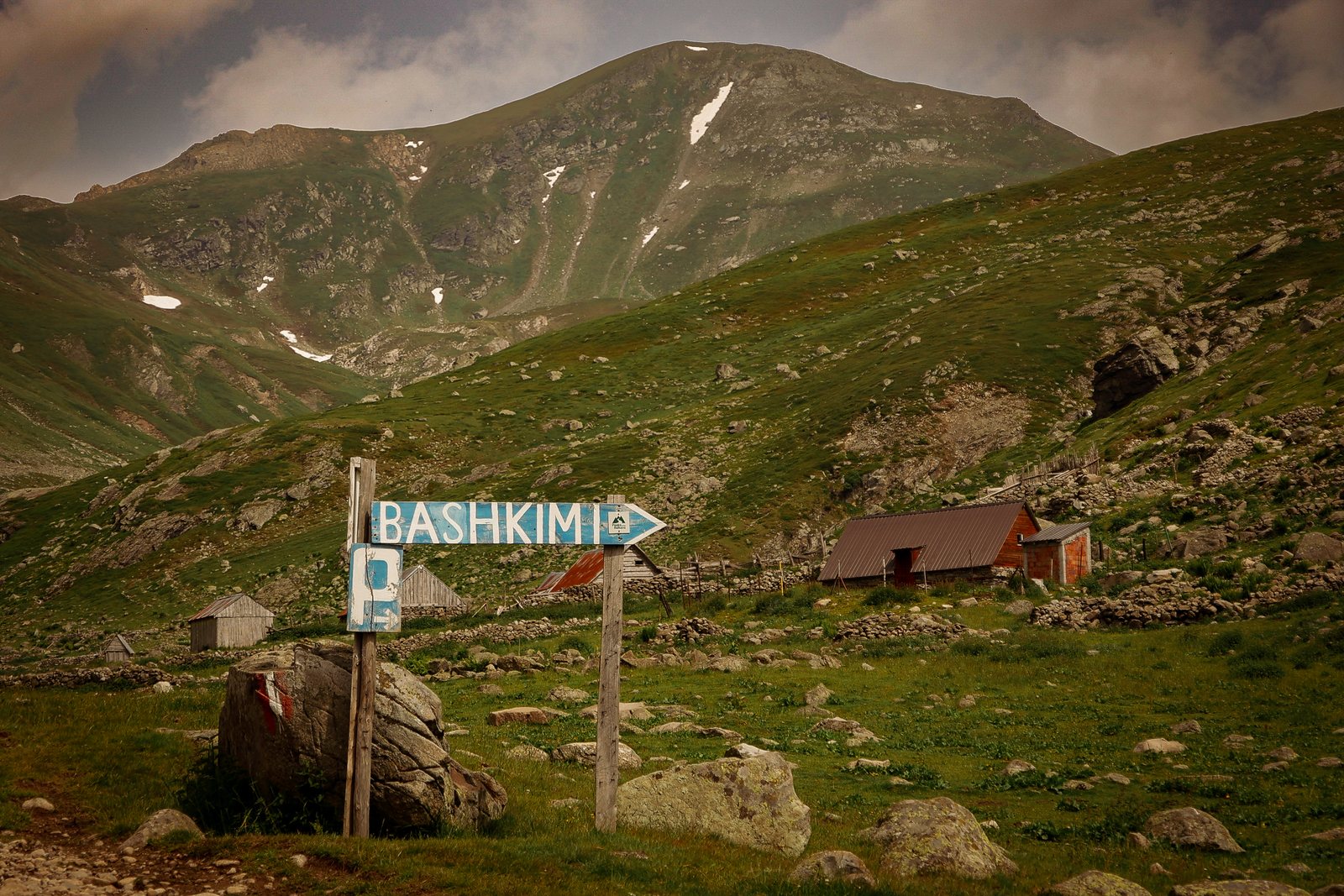 A trail sign pointing toward a hut in a green valley