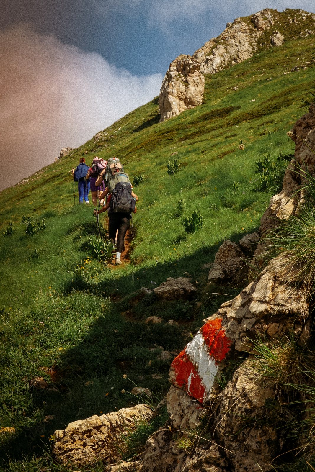 Hikers climbing a steep slope past a red and white trail marker