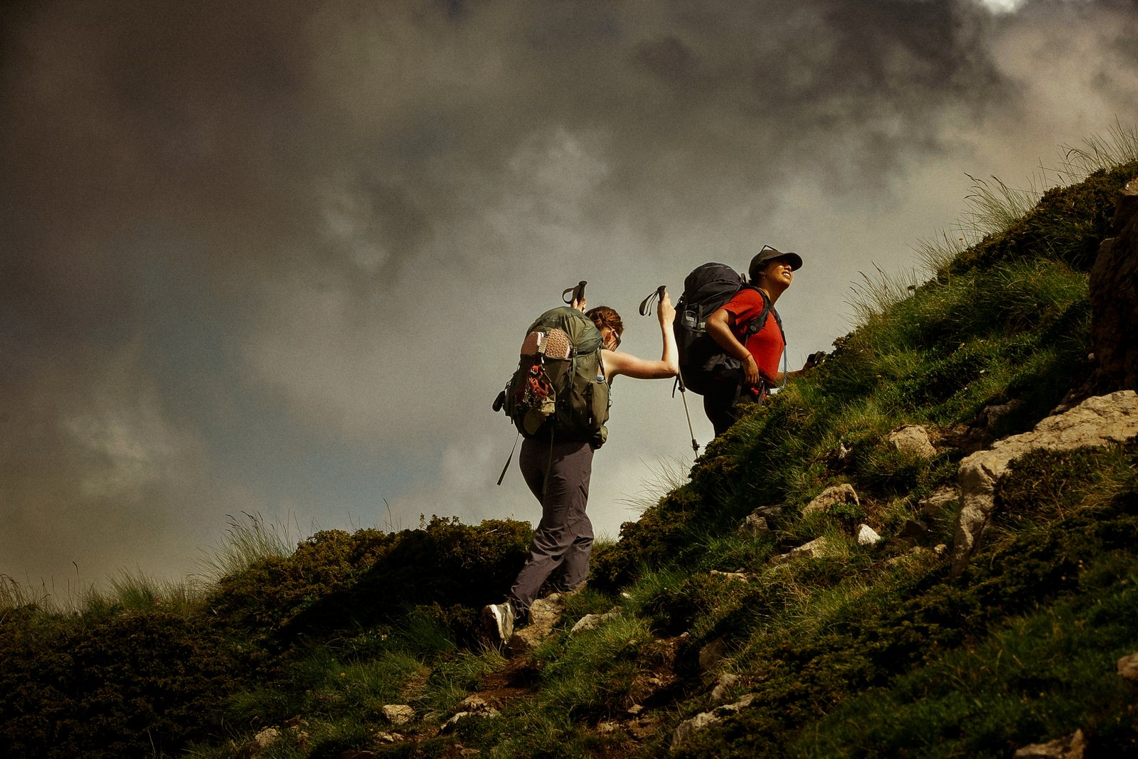 Hikers climbing a steep grassy slope under dark cloud