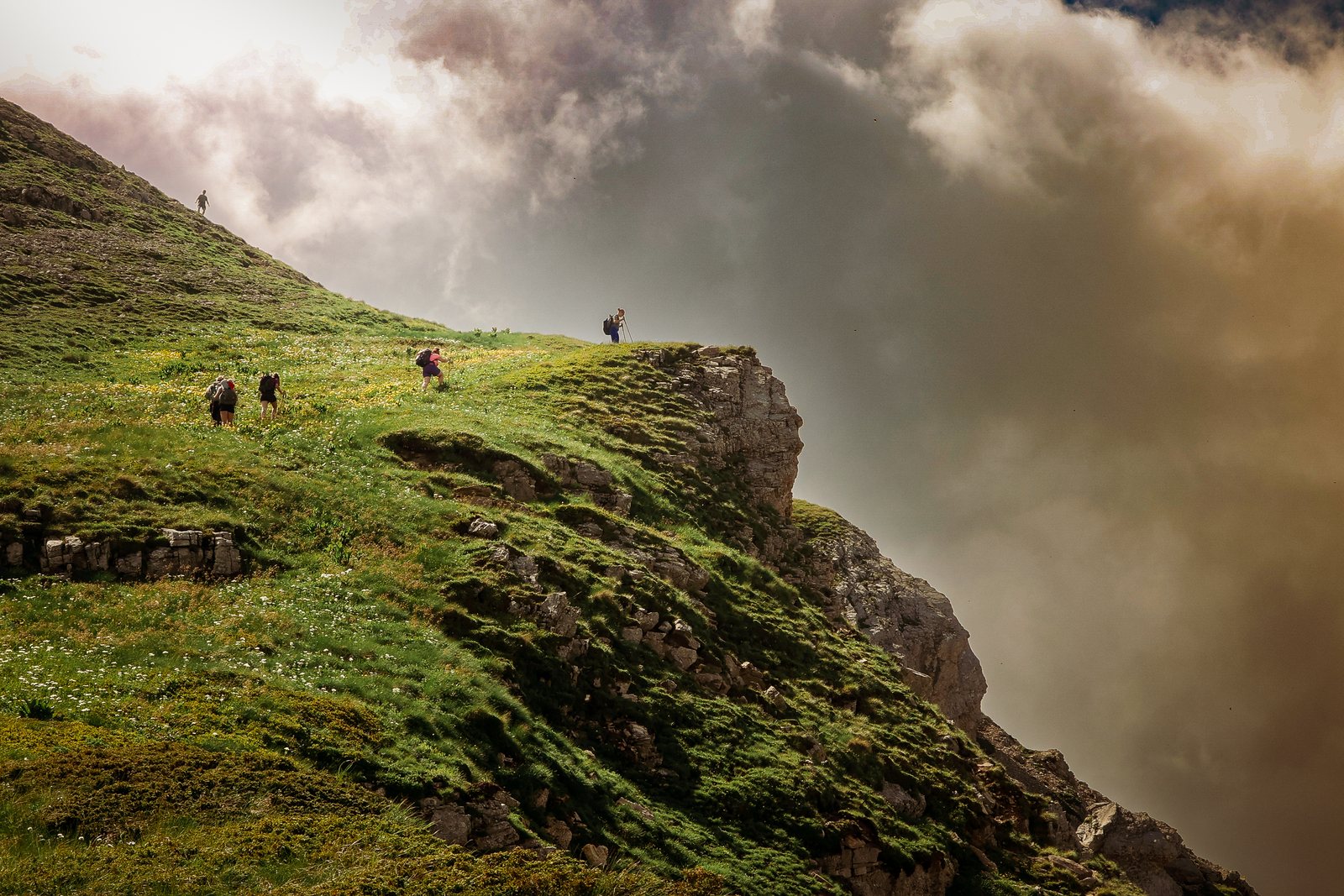 Hikers on a grassy cliff edge under a smoky sky