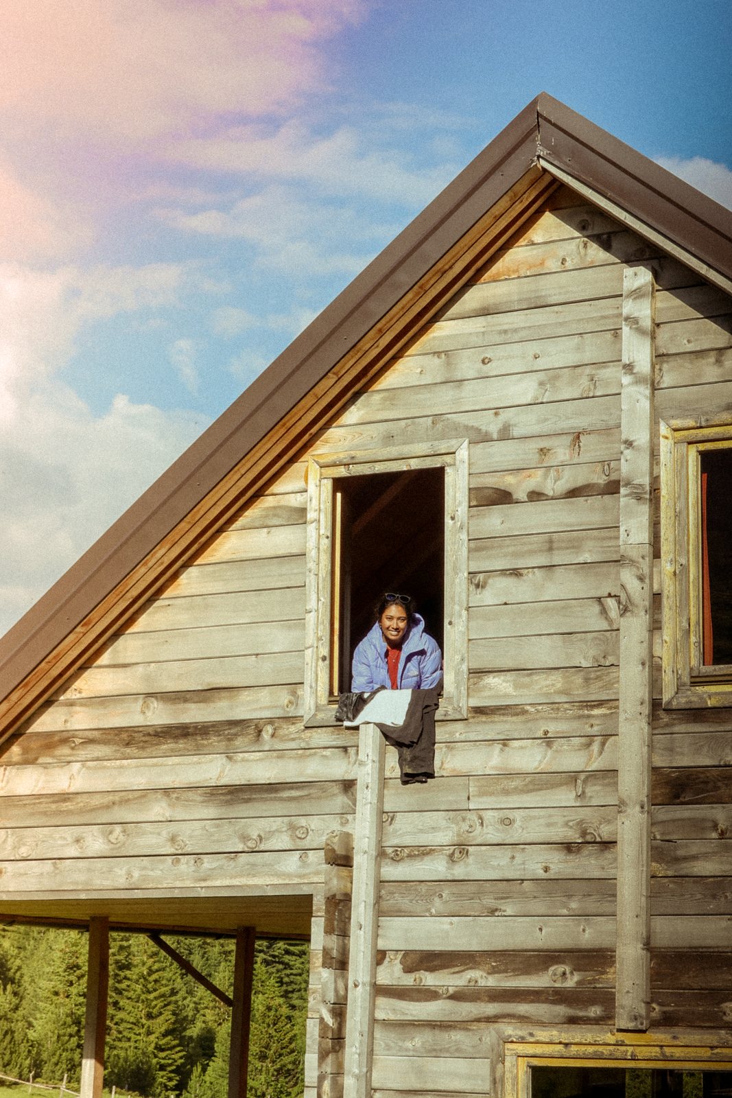 A hiker leaning out the window of a wooden hut