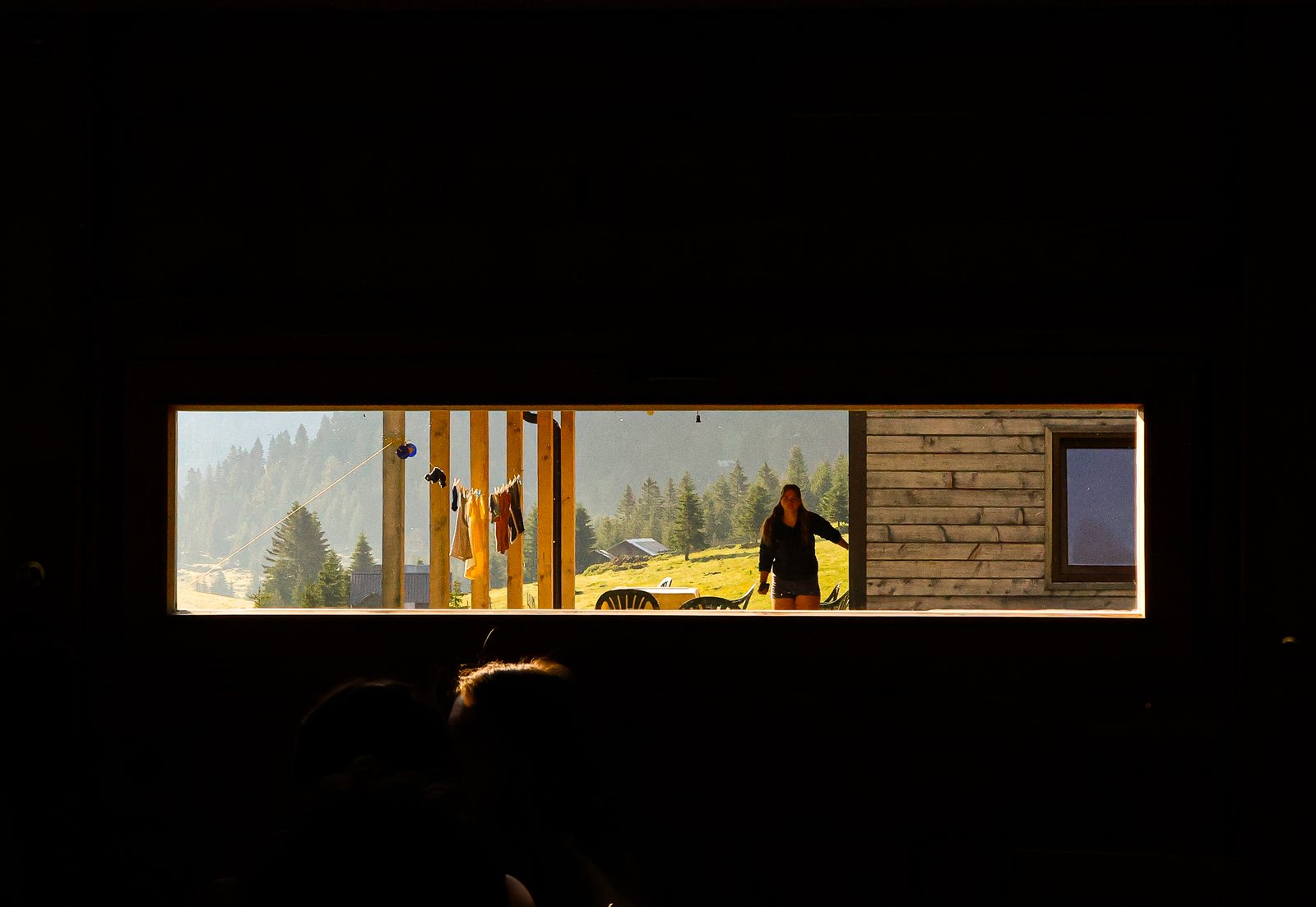 A hut window framing a hiker and pine trees outside