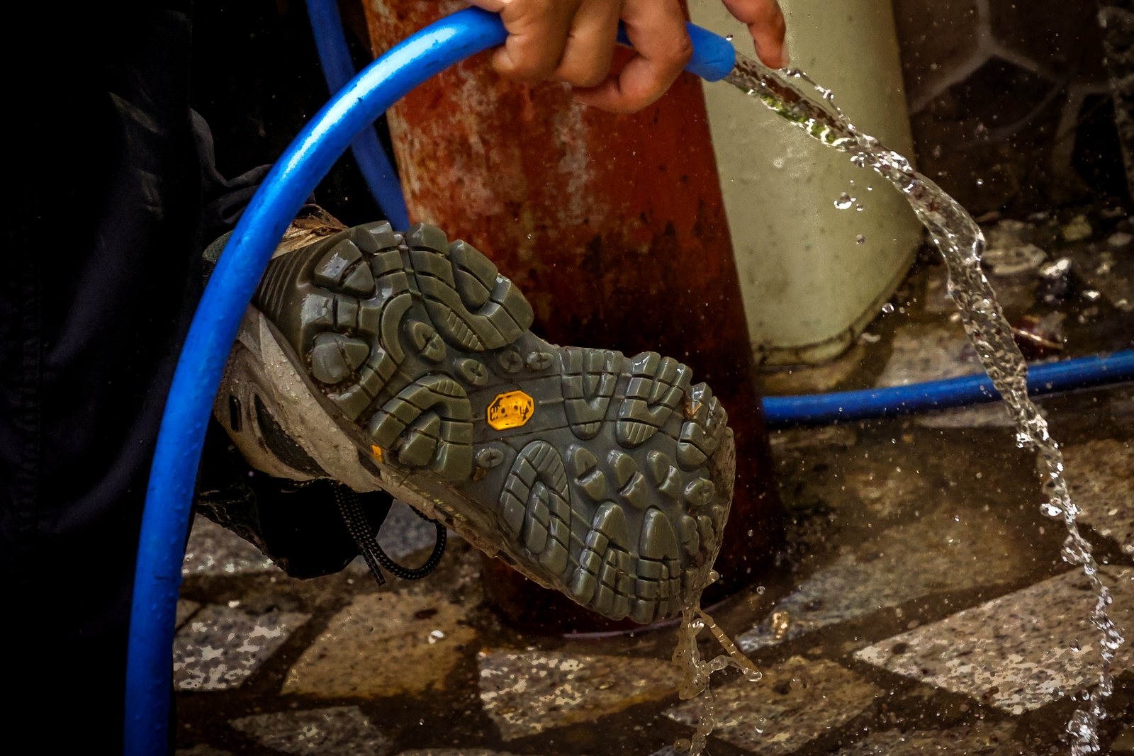 A hiking boot being rinsed with a hose