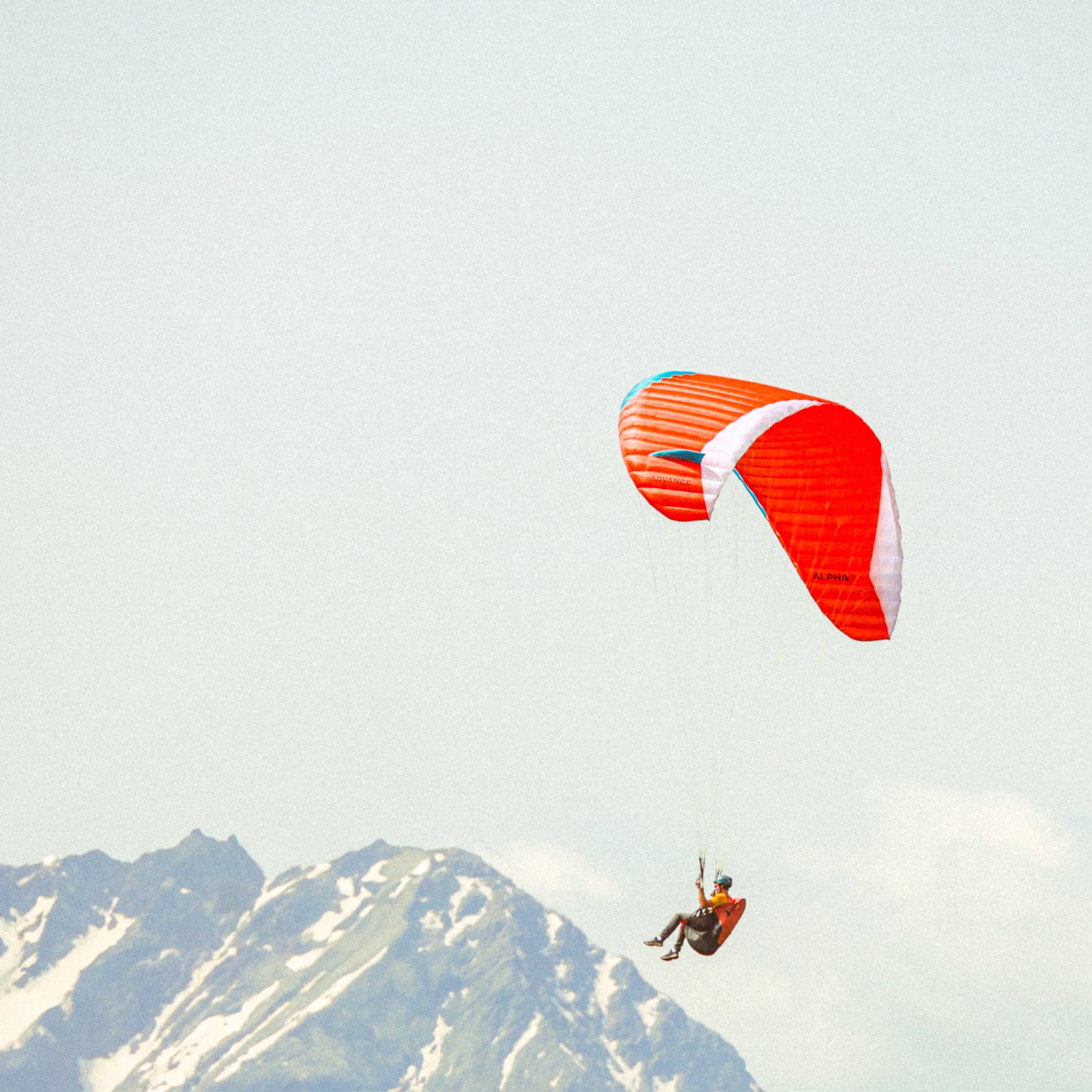A red paraglider drifting above a snowy peak