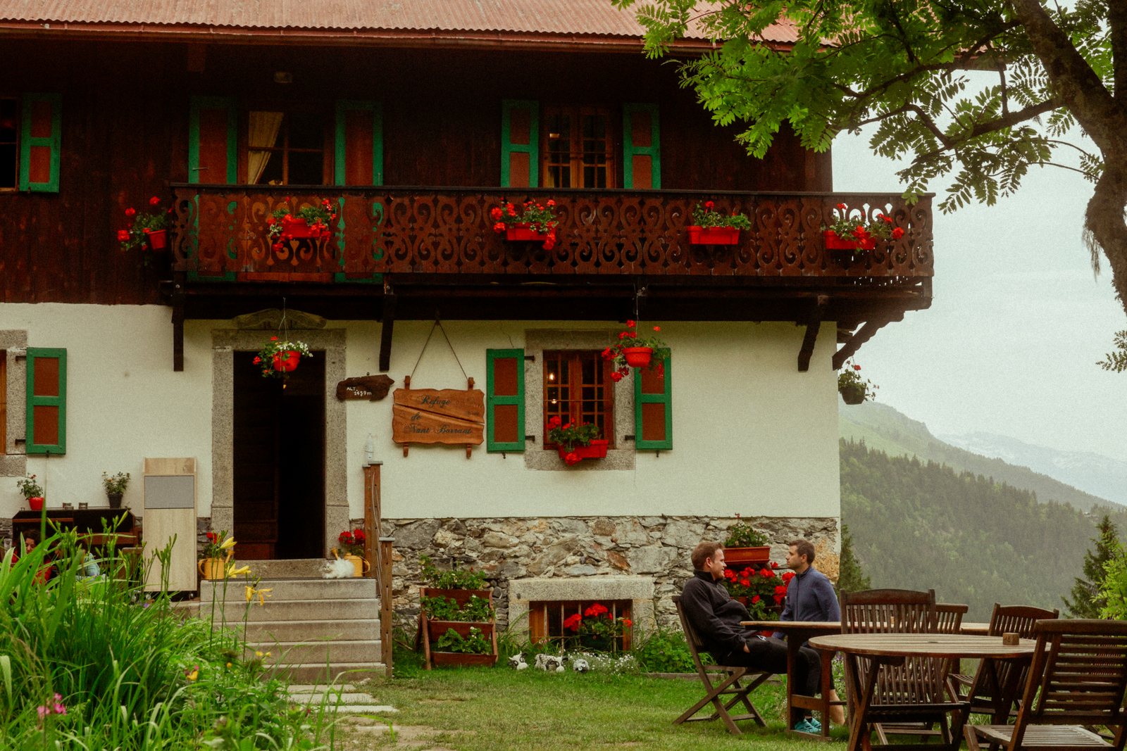 A chalet with red flower boxes and people at a table