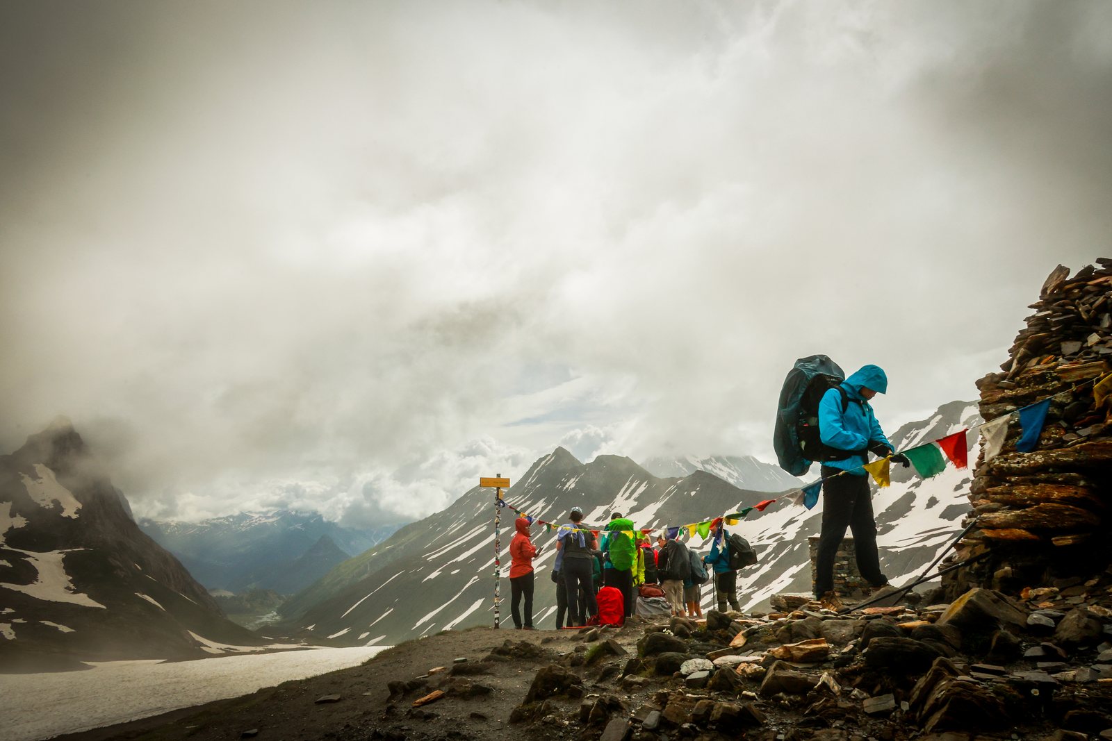 Hikers at a cairn strung with prayer flags, peaks behind