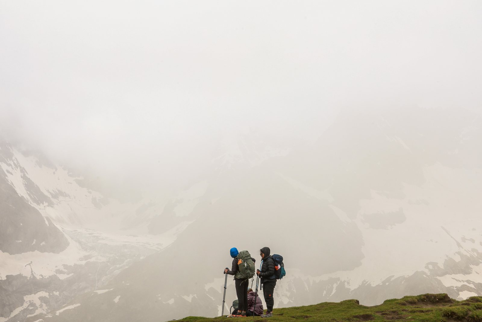 Two hikers pause on a ridge in thick cloud