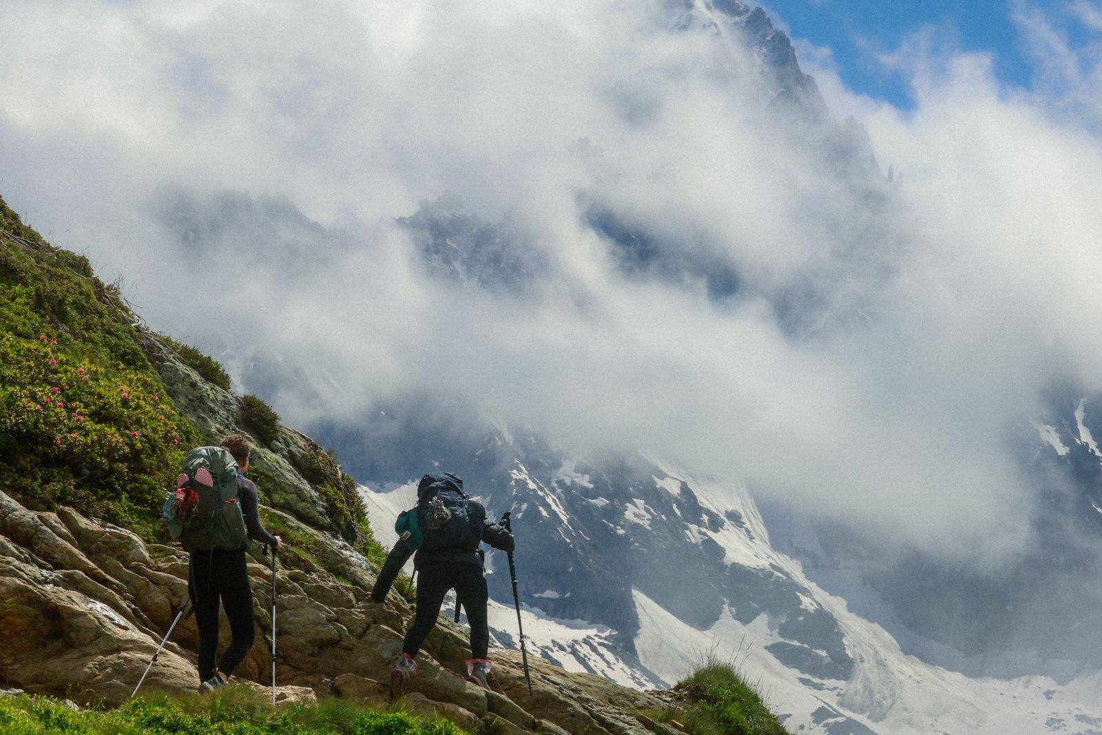 Two hikers climbing a rocky trail beside a glacier
