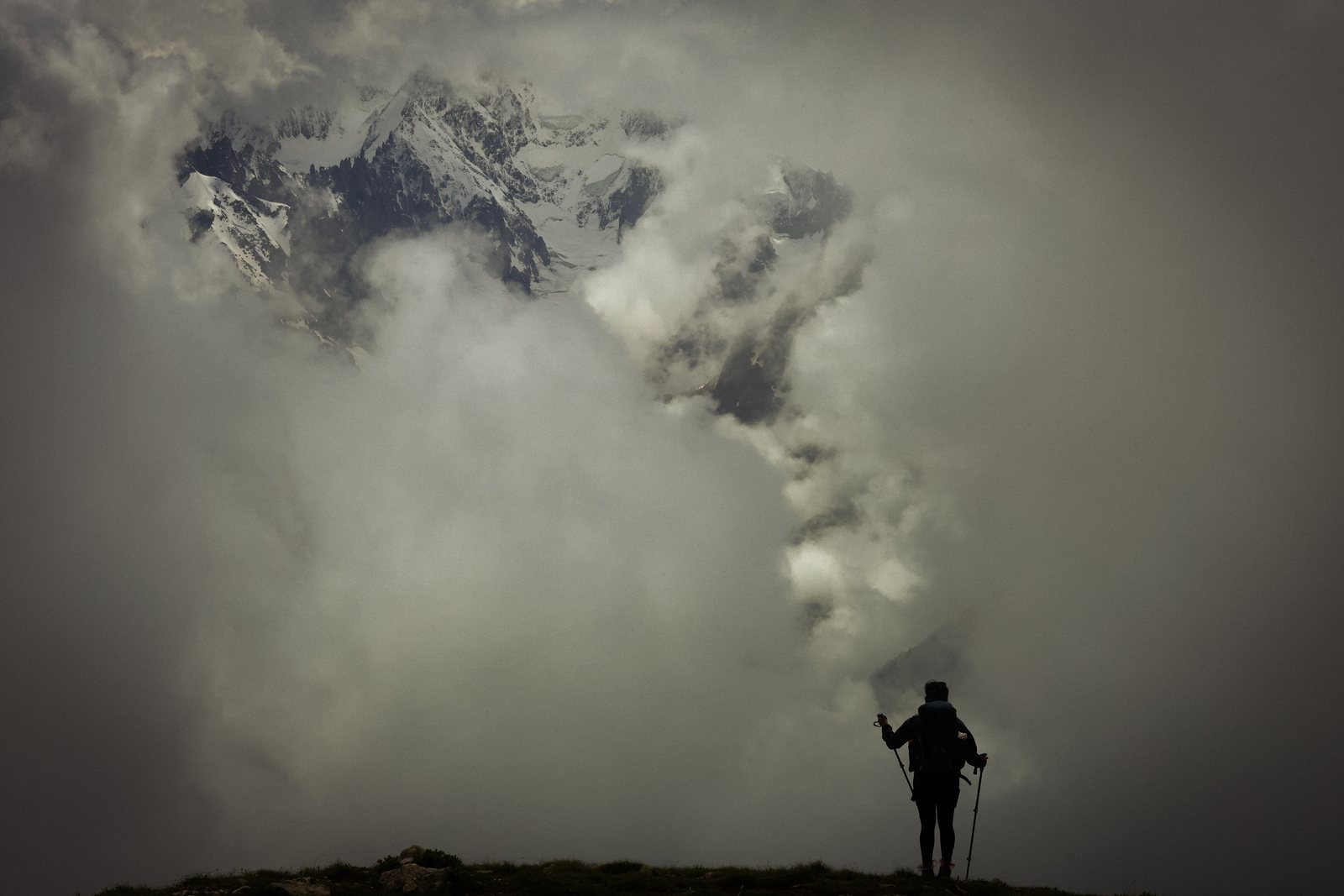A hiker silhouetted on a ridge as cloud pours over the peaks