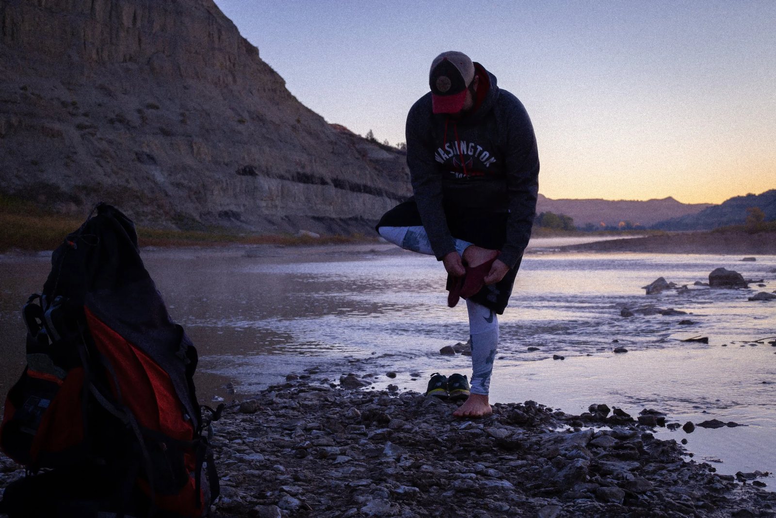 A hiker stretching on a rocky riverbank at dusk