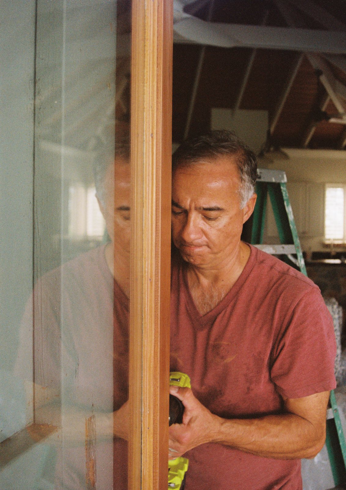 A man working at a wooden window frame, reflected in the glass