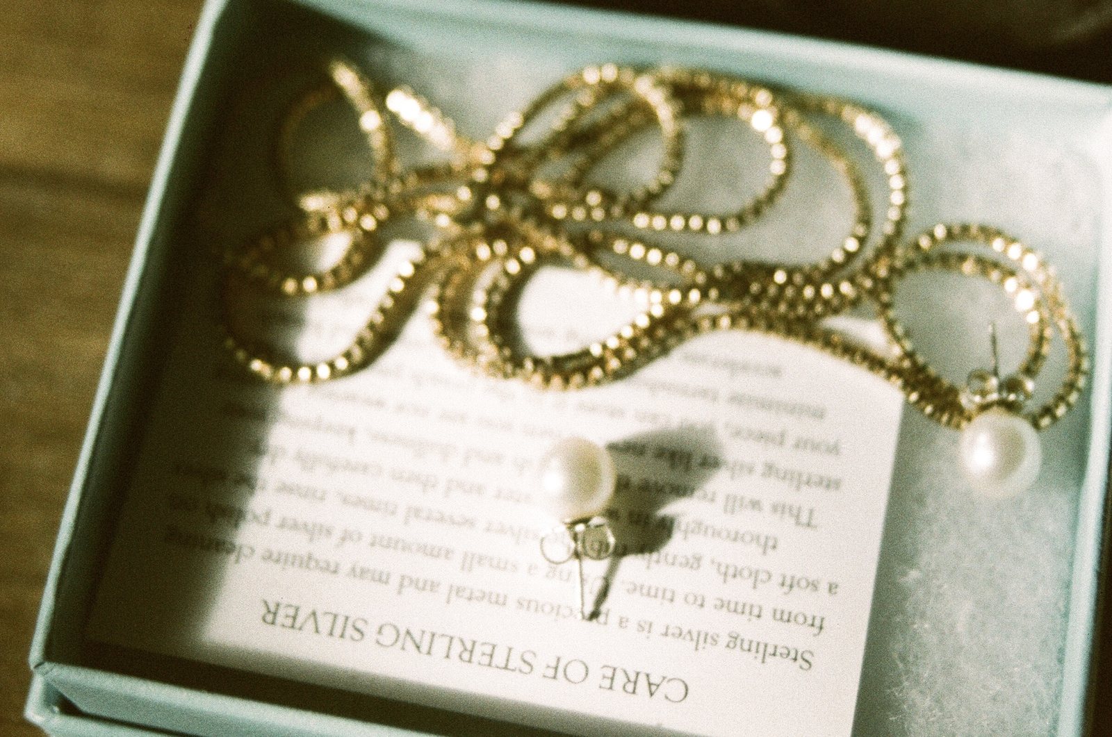 A gold chain and pearl earrings in a gift box