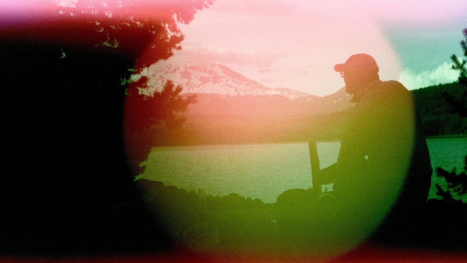 A man looking at a snow peak across a lake, framed by a light leak